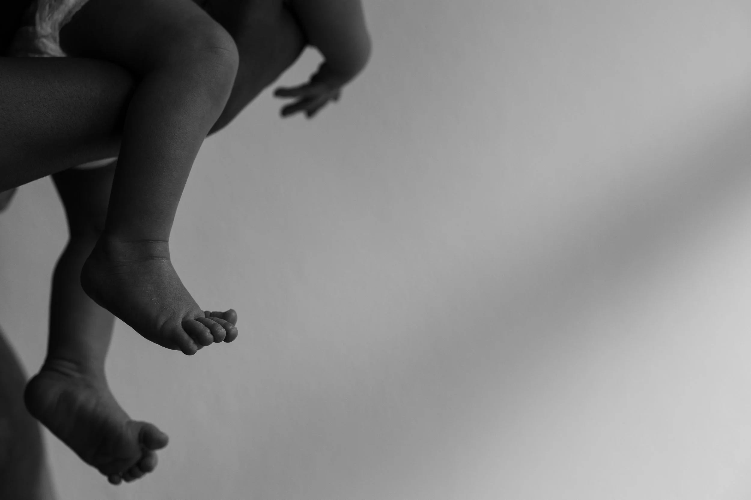 Schwarz-weiß-Fotografie einer Hand, die einen Babyfuß hält.