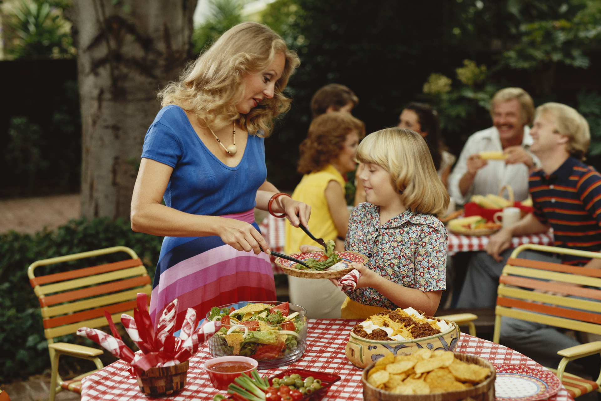 An image of a woman in the 1980s serving up a kid a plate of food at a picnic
