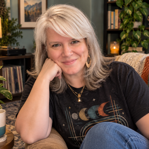 Carly Finseth, founder of Cozy Writing Co., smiling while seated in a cozy room with books and plants.