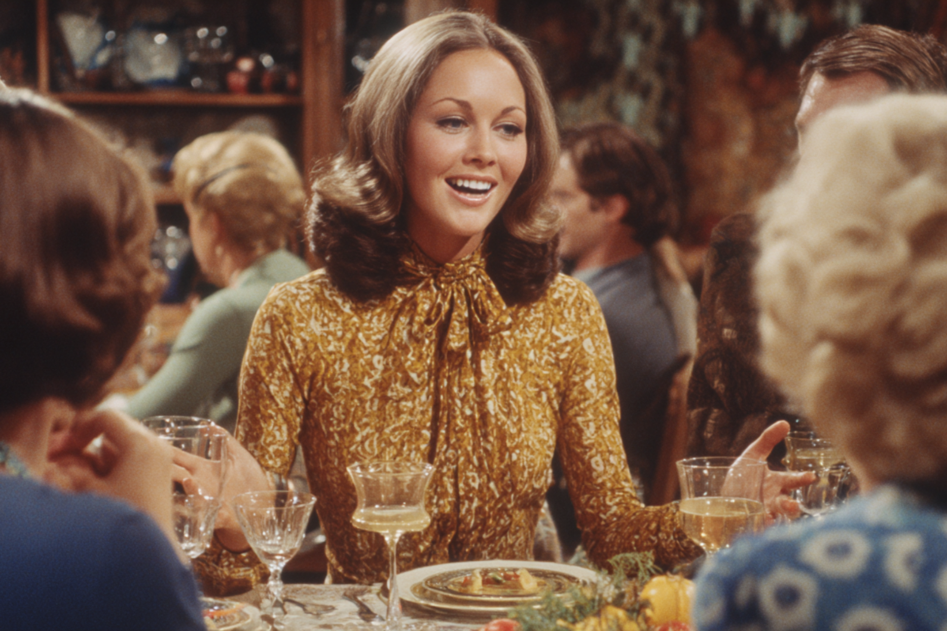 A woman speaking animatedly at a dinner table while others listen, suggesting a lively conversation and shared storytelling.