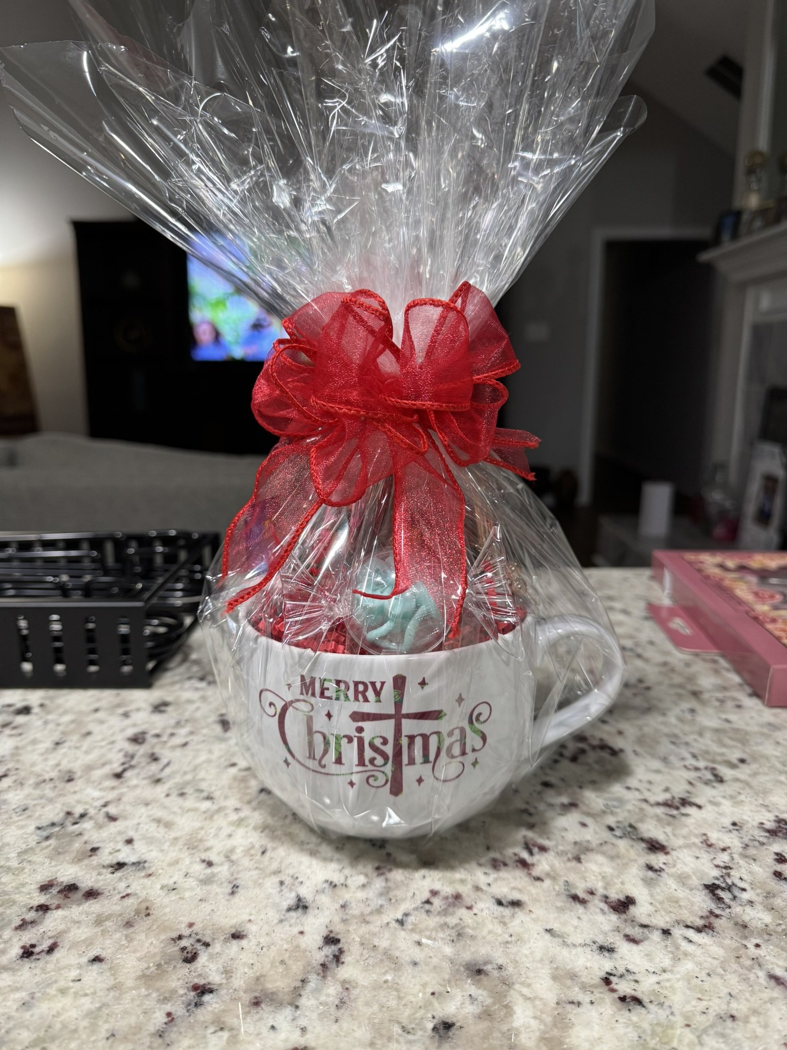 A Christmas-themed gift mug wrapped in clear plastic with a red ribbon bow, placed on a kitchen countertop.