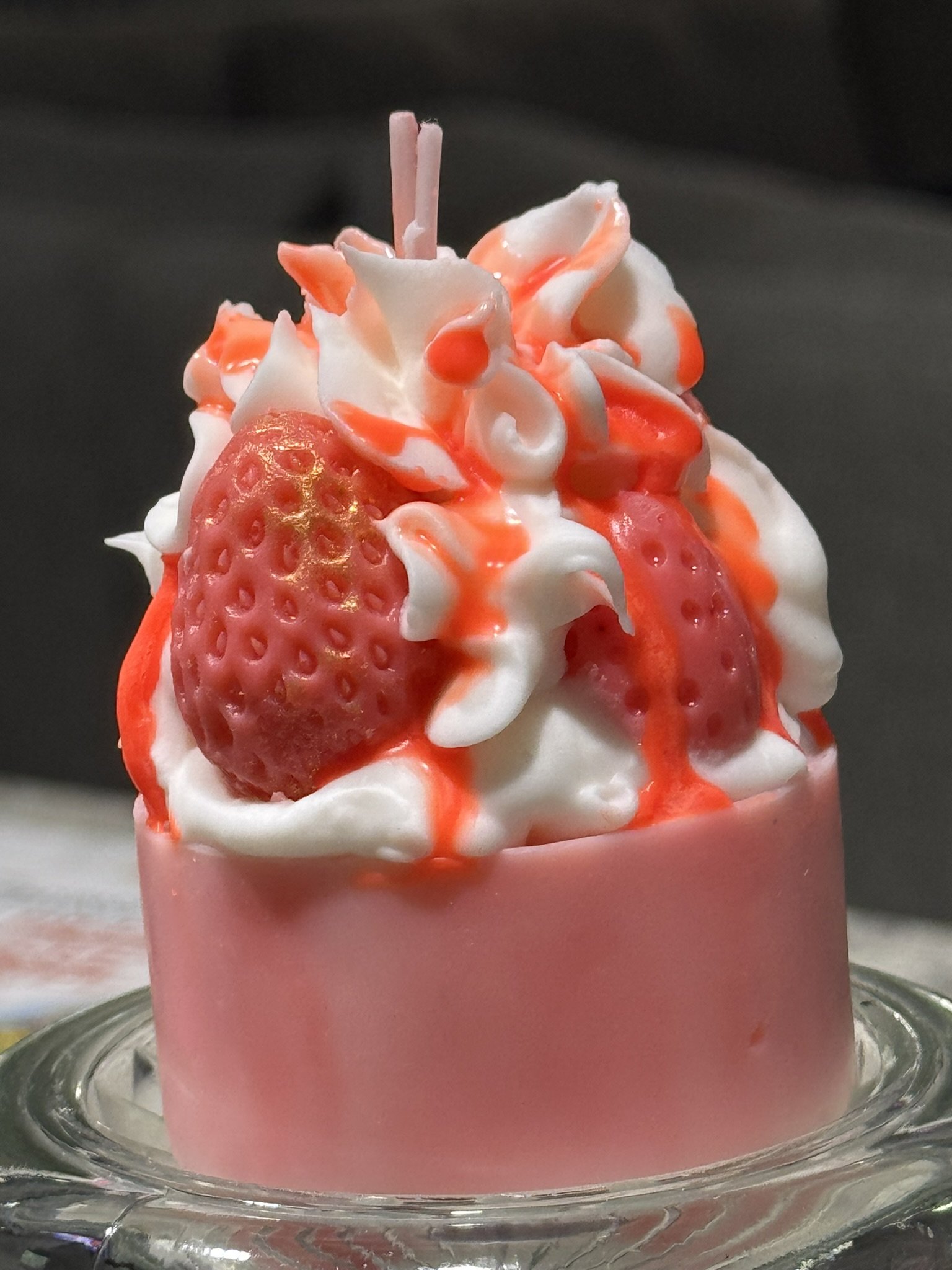 Close-up of a mini dessert with whipped cream, strawberries, and strawberry syrup in a pink cup