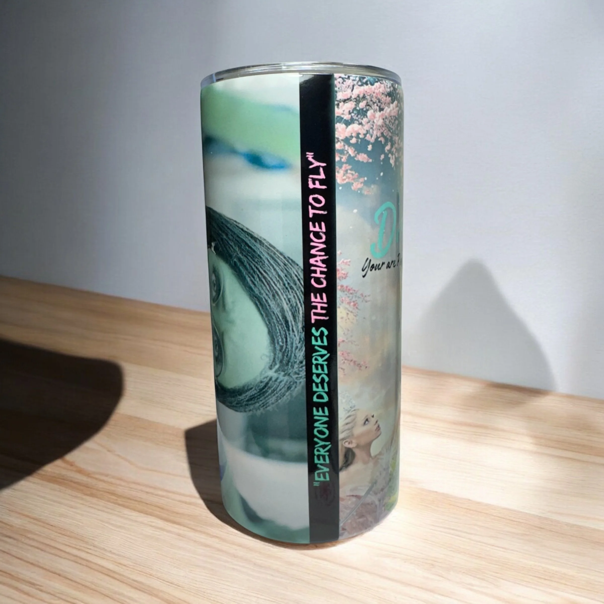 A tall clear tumbler with a colorful design including a woman, a wave, cherry blossoms, and the words 'Everyone deserves the chance to fly' written vertically.