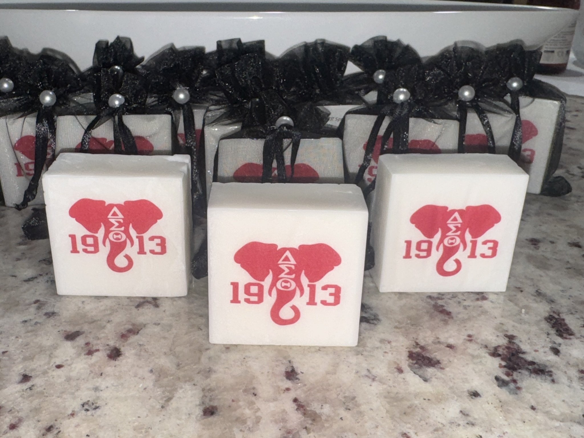 White cube-shaped soap with DST (Delta Sigma Theta)  red elephant graphic and the year 1913 printed on them, placed on a speckled countertop.