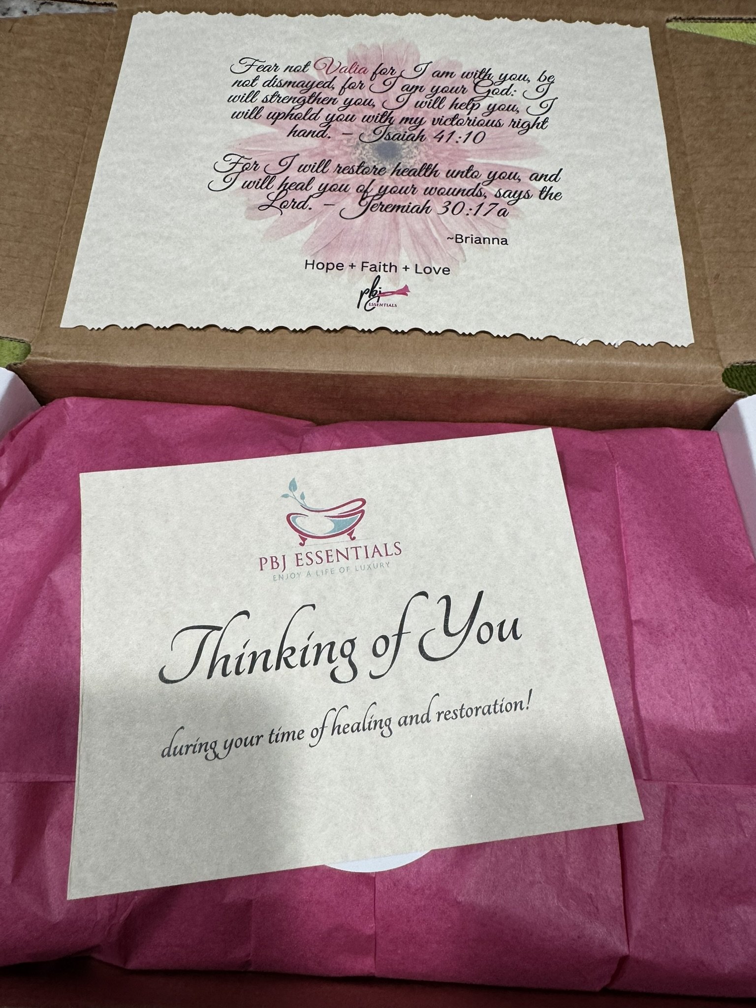 A pink tissue paper-lined box with a card that says "Thinking of You during your time of healing and restoration!" and an inner lid with a message about faith, hope, and love from Brianna.