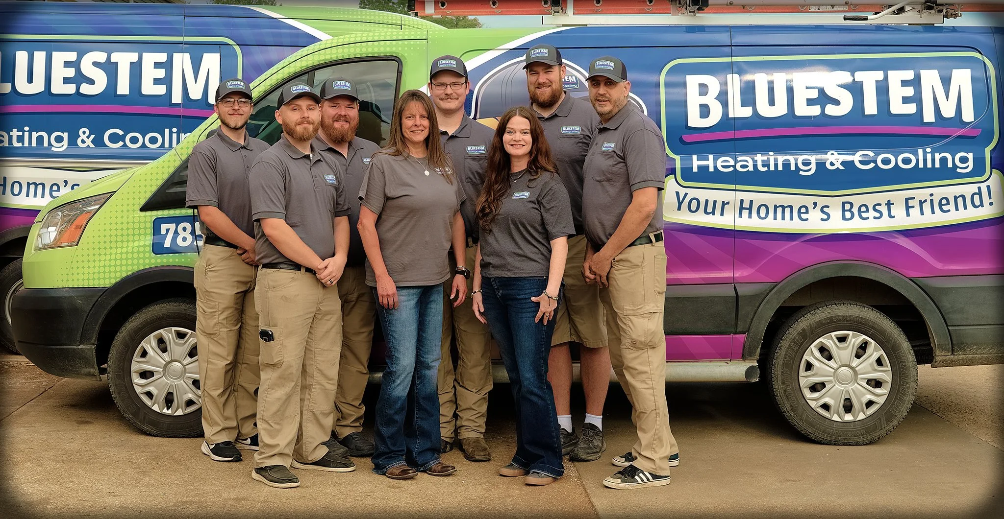 Group of seven people standing in front of a colorful company van with 'Bluestem Heating & Cooling' logo and slogan.