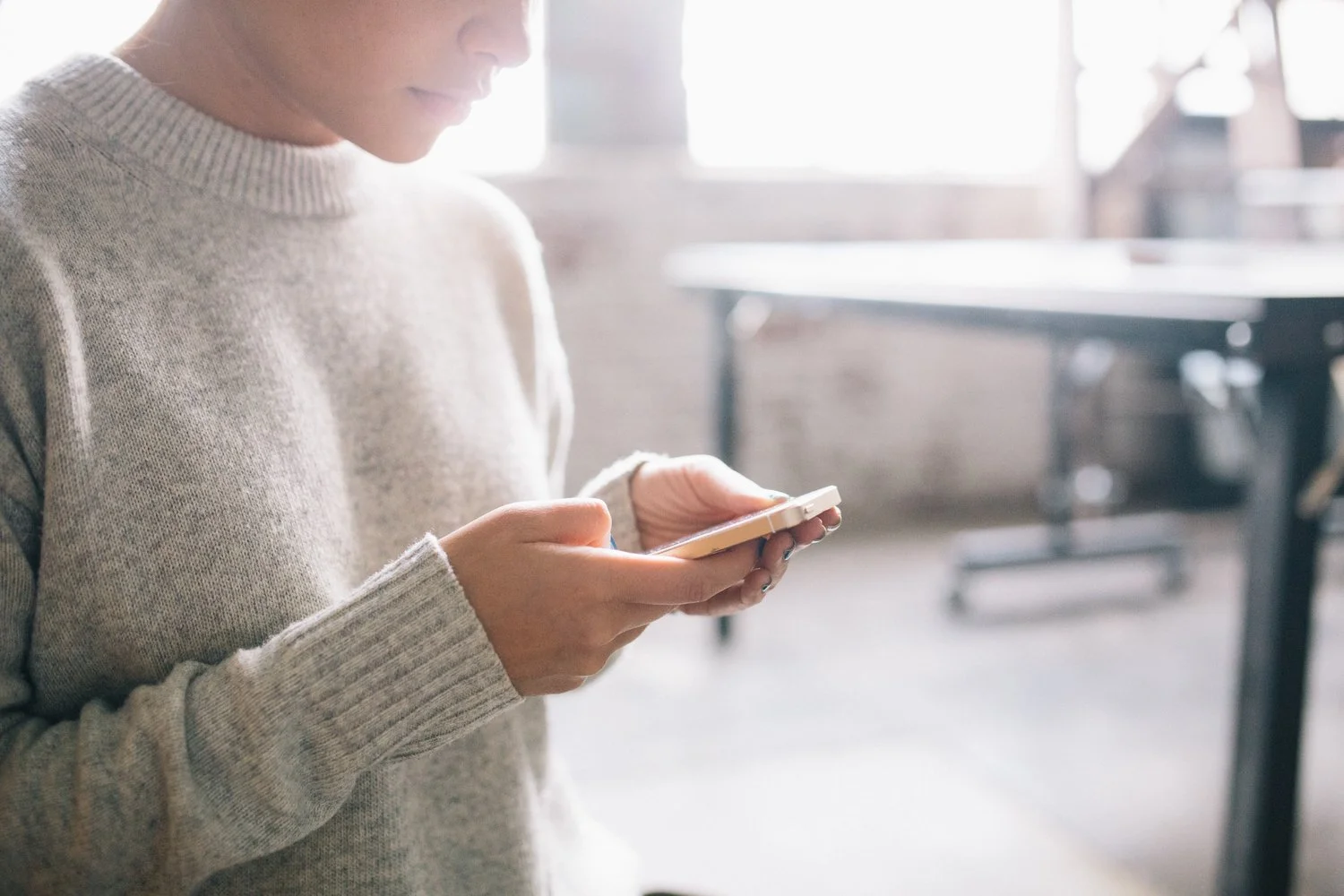 Person using a smartphone indoors, wearing a gray sweater.