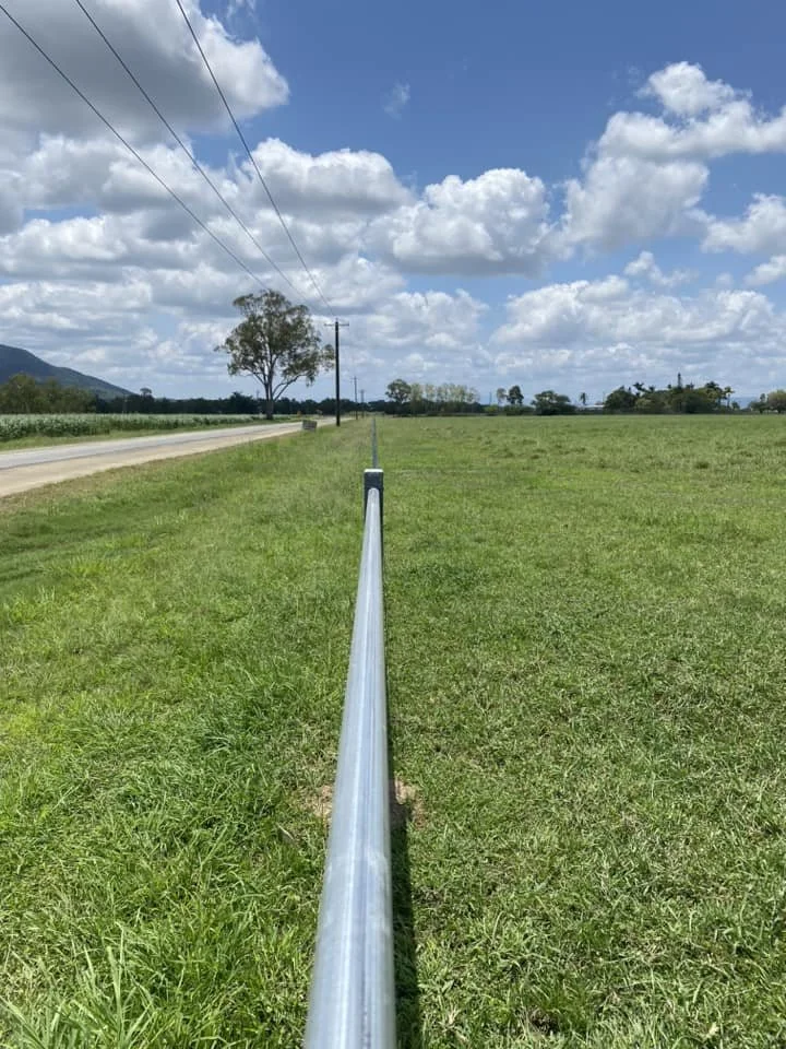 A long metal post with wires extending from it across an open grassy field, under a partly cloudy sky.