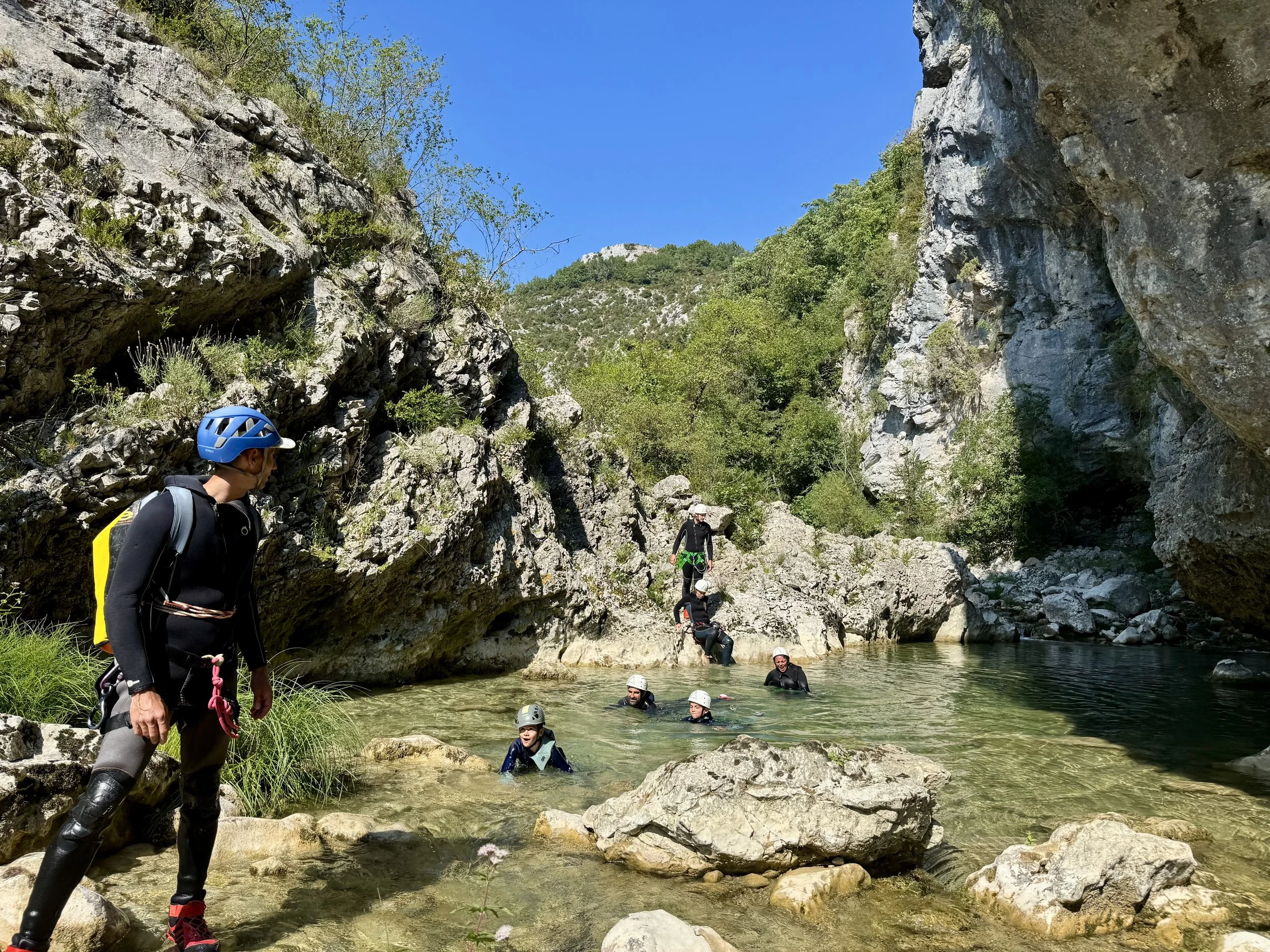 Le guide ouvre la voie dans un canyoning initiation pour une famille avec des enfants de tout âge qui sont en train de nager au soleil. 