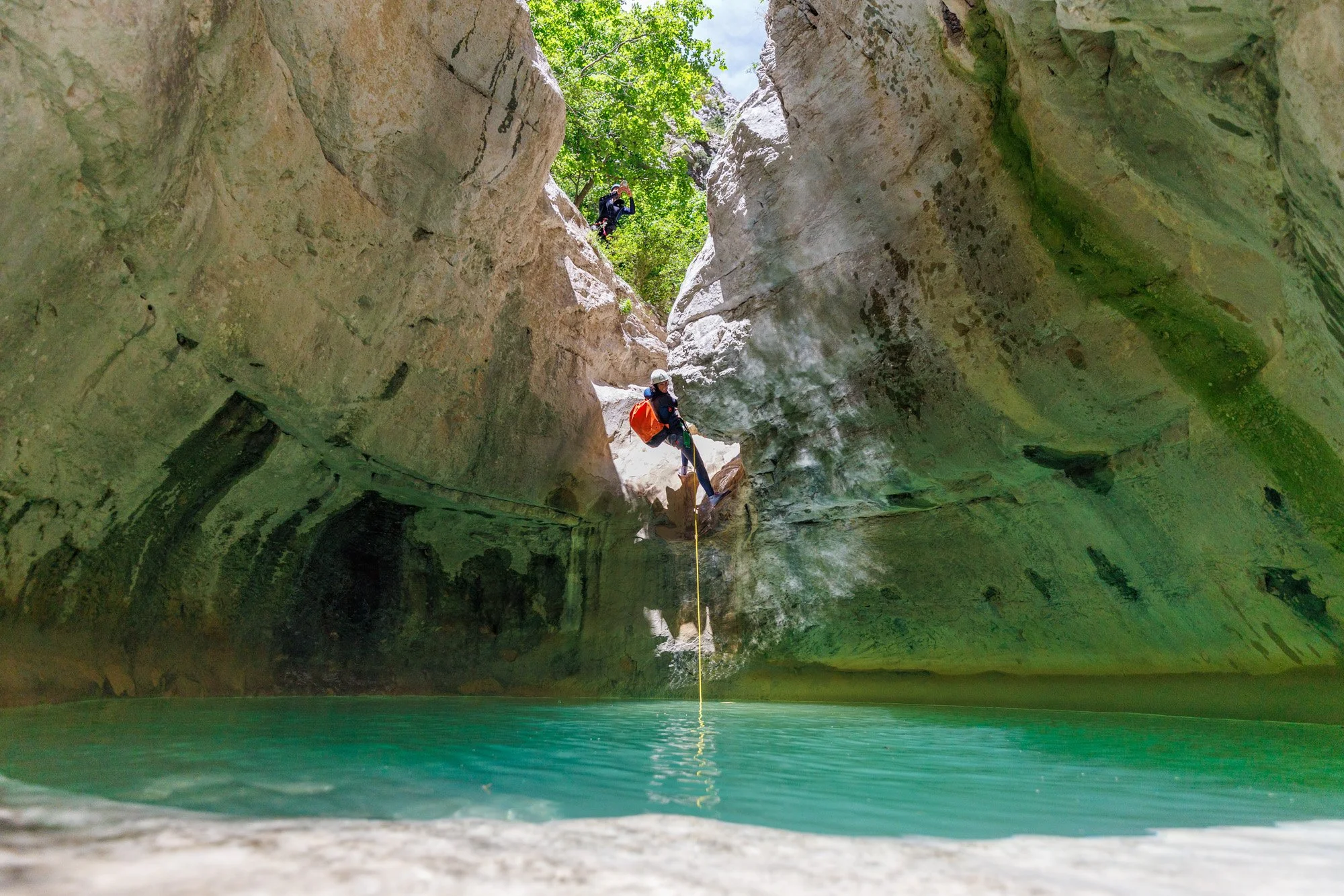 Descente en rappel au cœur d’un canyon rocheux vers une eau turquoise
