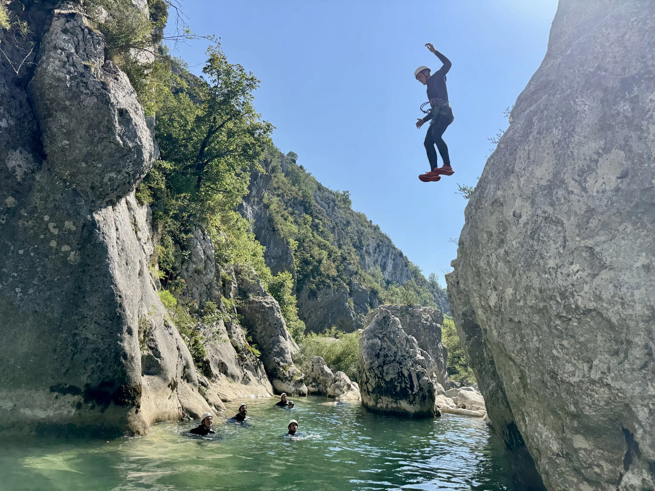 Une personne saute les autres la regardent depuis l'eau au soleil
