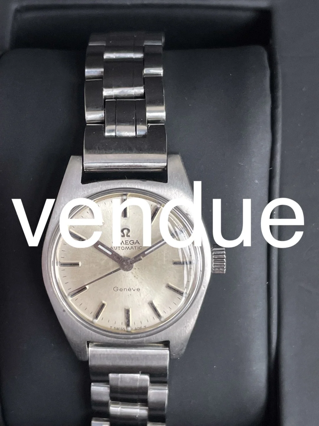 Montre Omega vintage en acier avec un bracelet métallique, cadran blanc, aiguilles noires, et chronomètre. La montre indique 9:44:09.