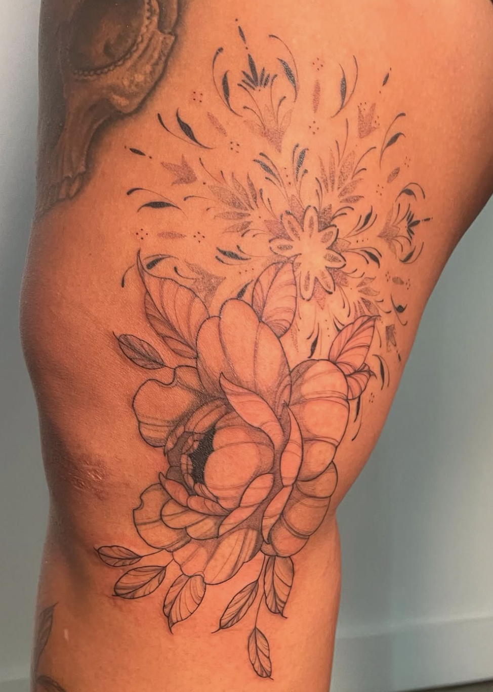 A black outline tattoo of a rose with leaves on a person's upper arm, with a floral and abstract design above it.