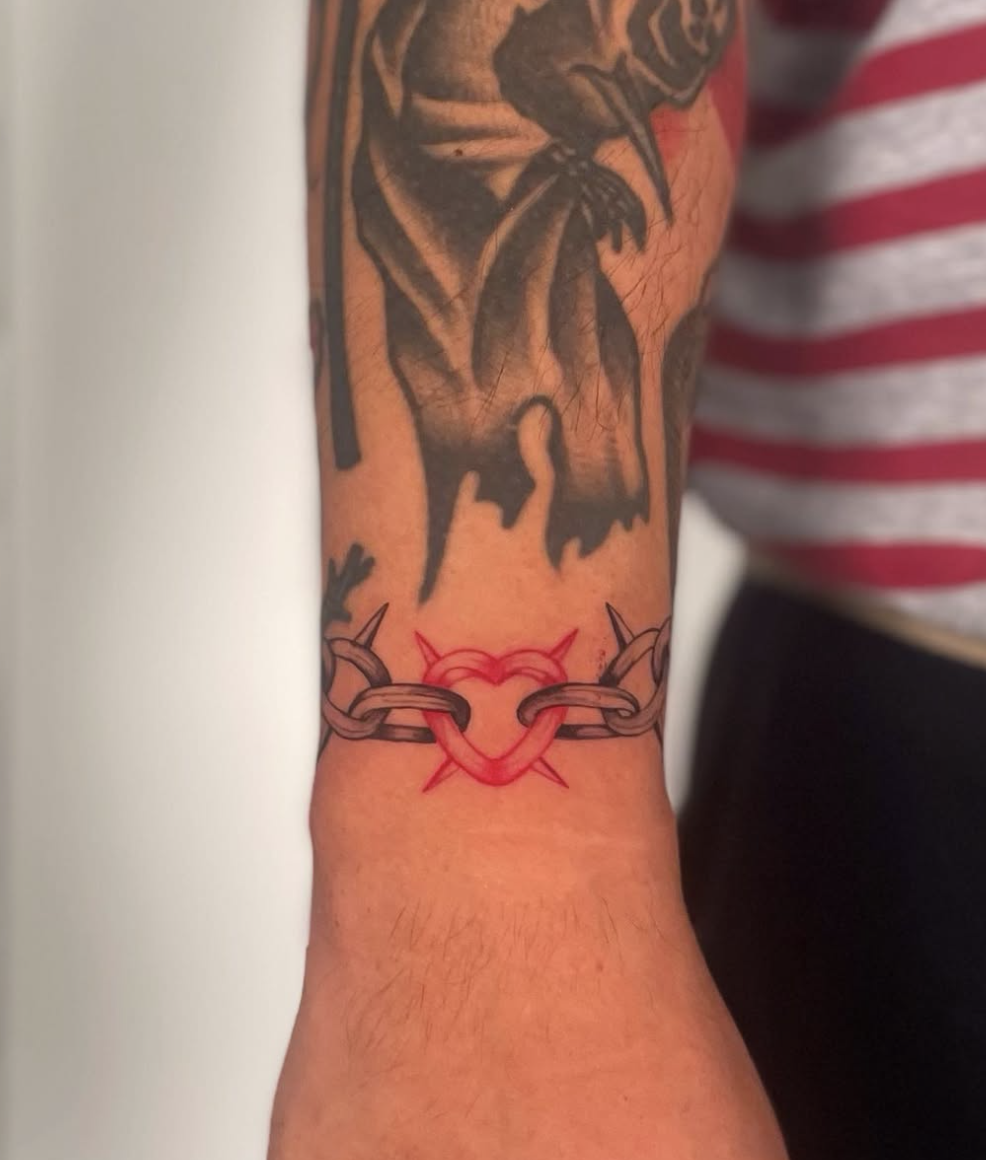 Tattoo of a chain with a red heart-shaped padlock and spikes on the wrist.