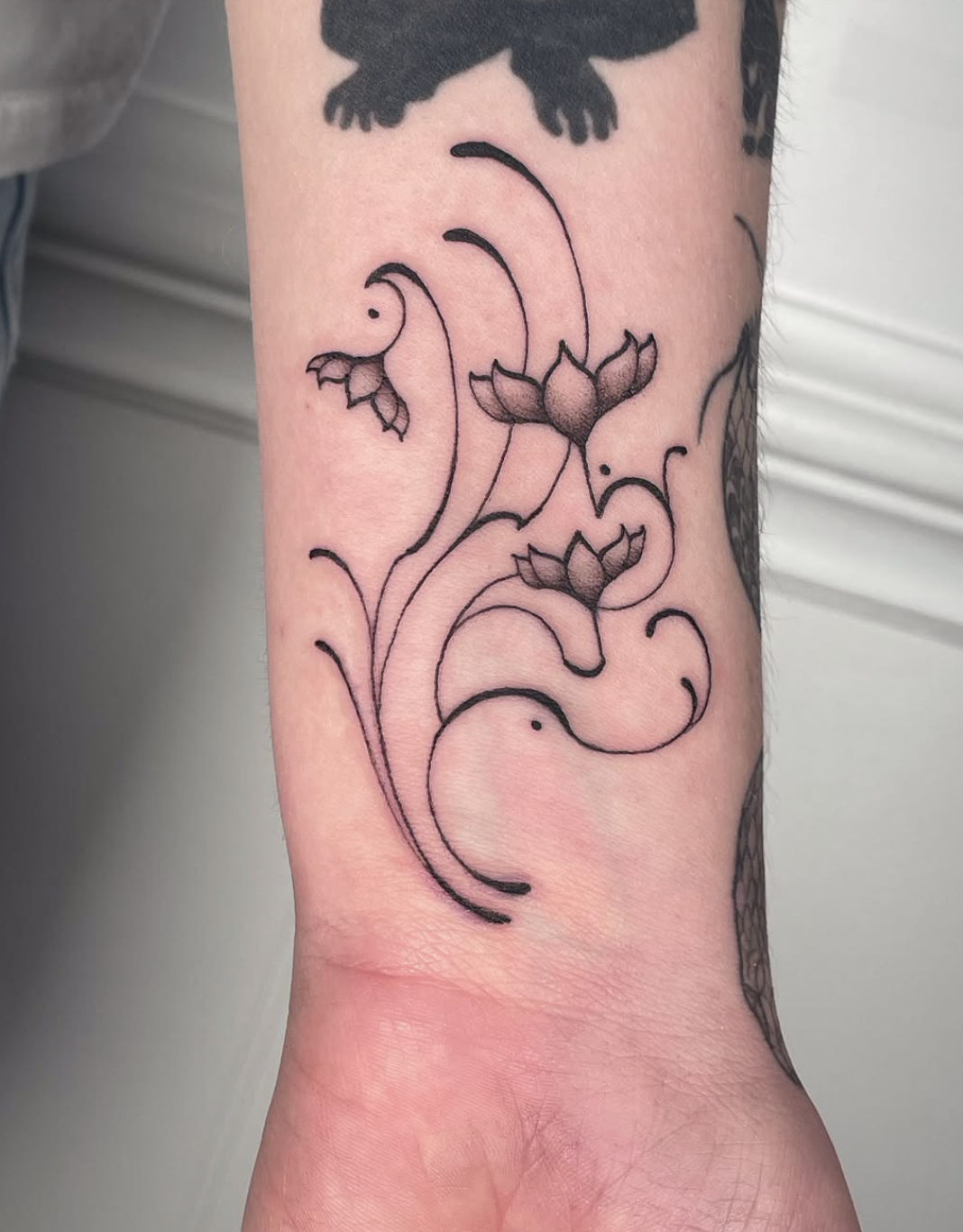 A black outline tattoo of lotus flowers and swirling lines on a person's inner forearm.