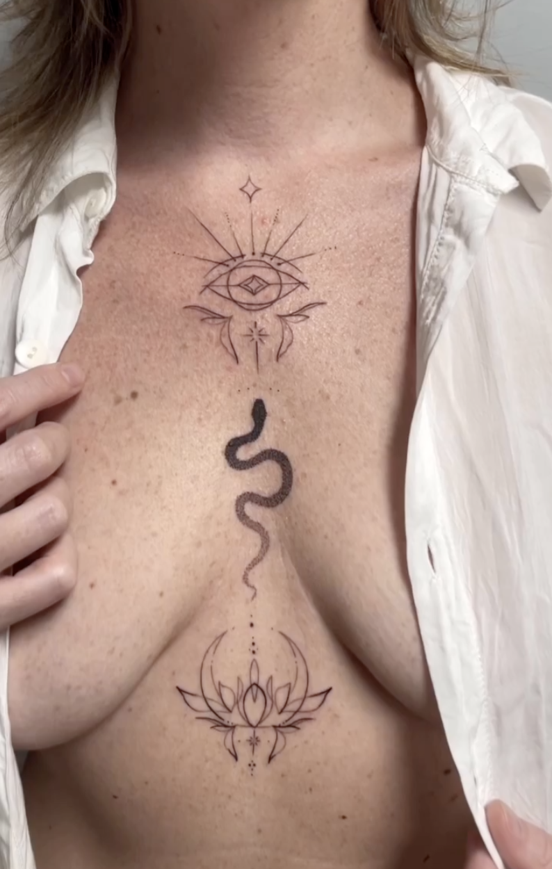 Tattoo on a person's chest featuring geometric designs, an eye, a snake, and a lotus flower.