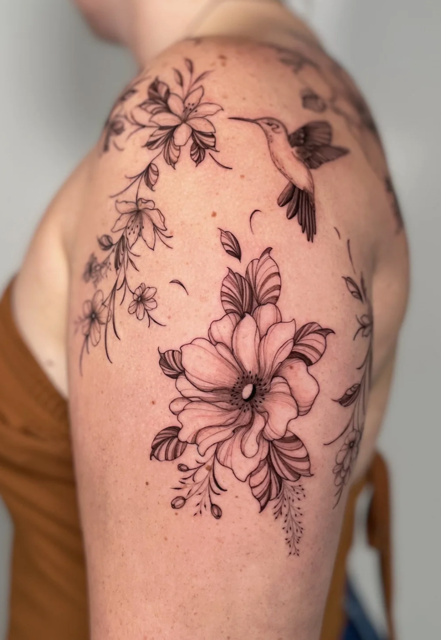 Black and gray floral tattoo with a hummingbird on a person's upper arm.