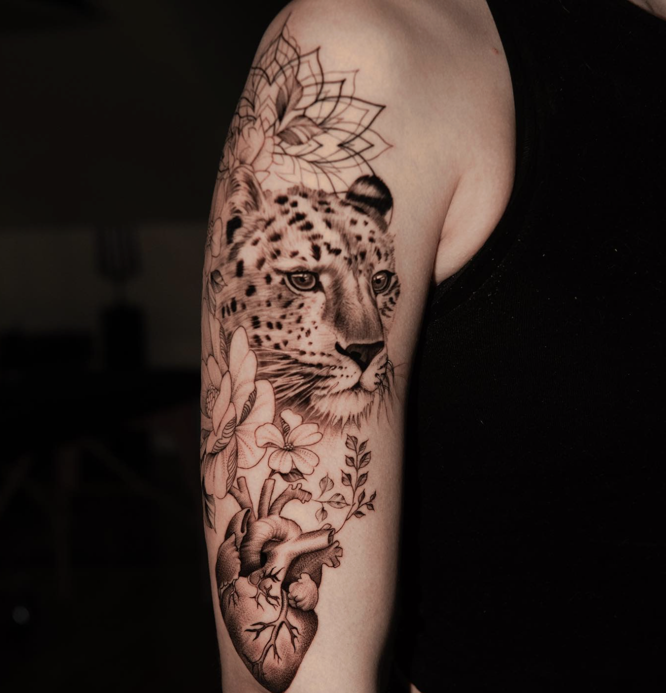 Tattoo of a leopard's face, surrounded by flowers and a human heart on a person's upper arm.