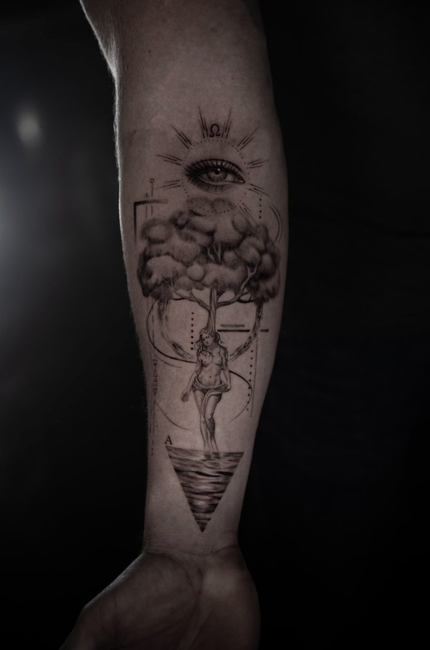 A tattoo of a woman walking over water, with a tree on her head, an eye with the Omega symbol above it, and abstract geometric shapes.