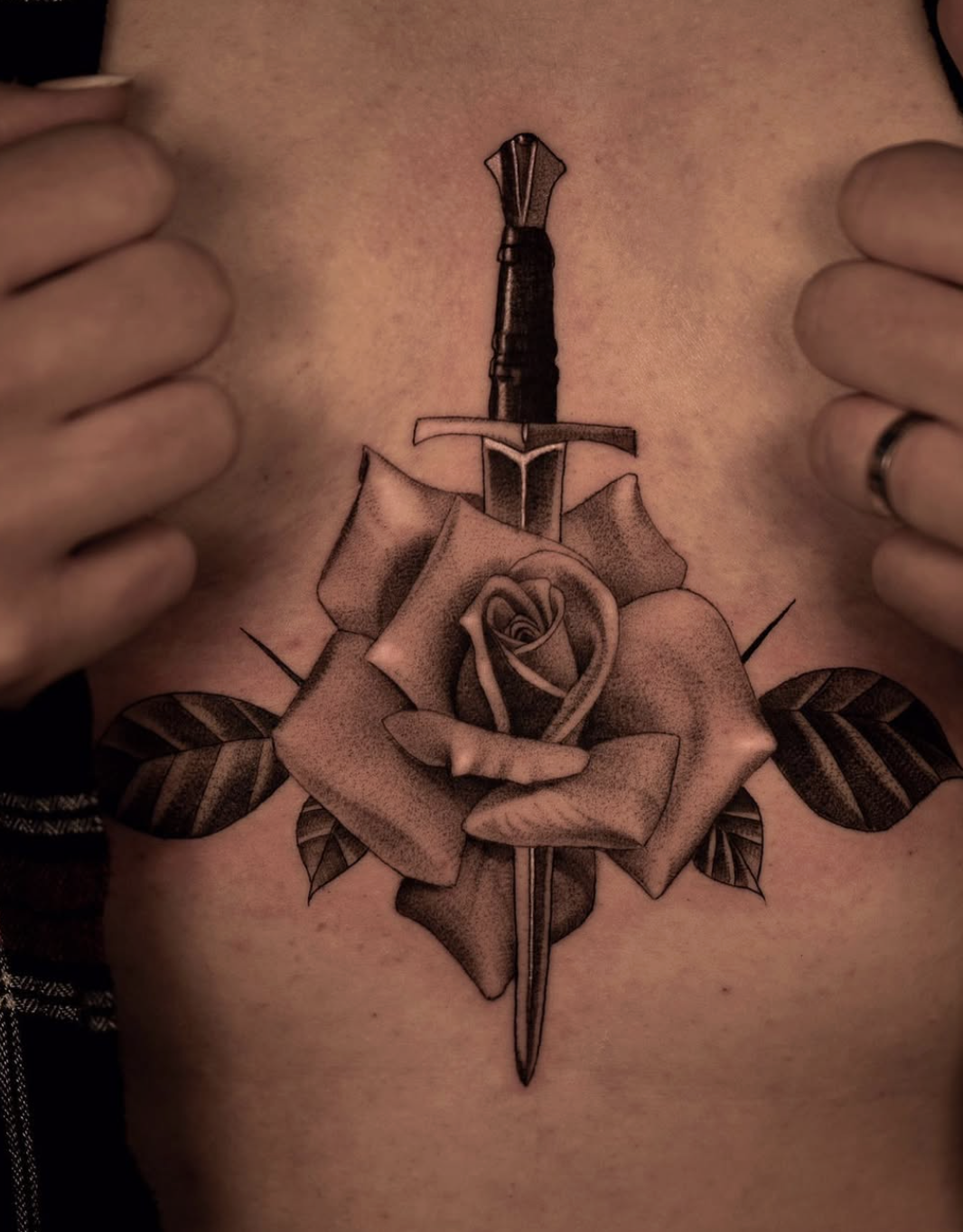 Tattoo of a sword piercing a rose with leaves.
