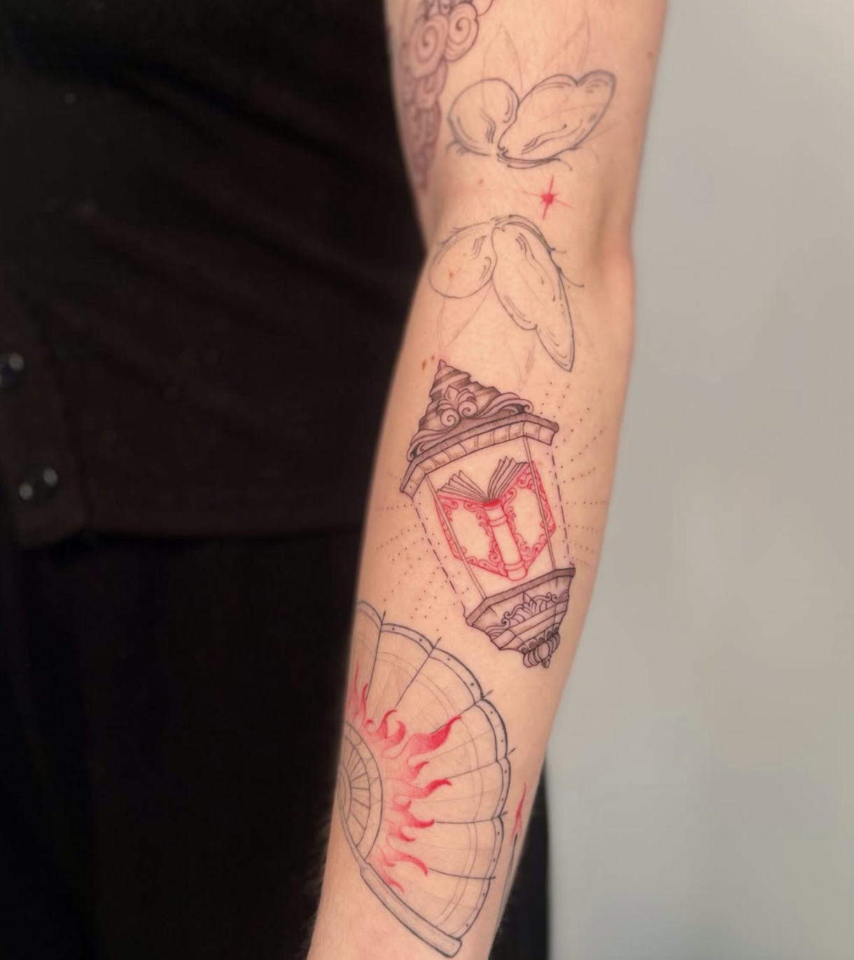 Tattoo featuring a butterfly, a star, an lantern with an open book inside, and a semi-circular design with red flames or rays.