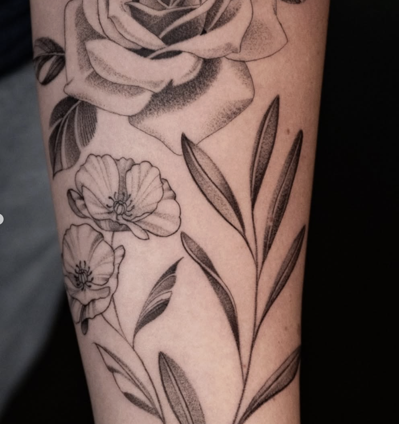 Black and gray floral tattoo featuring a rose at the top, with smaller flowers and leaves below.
