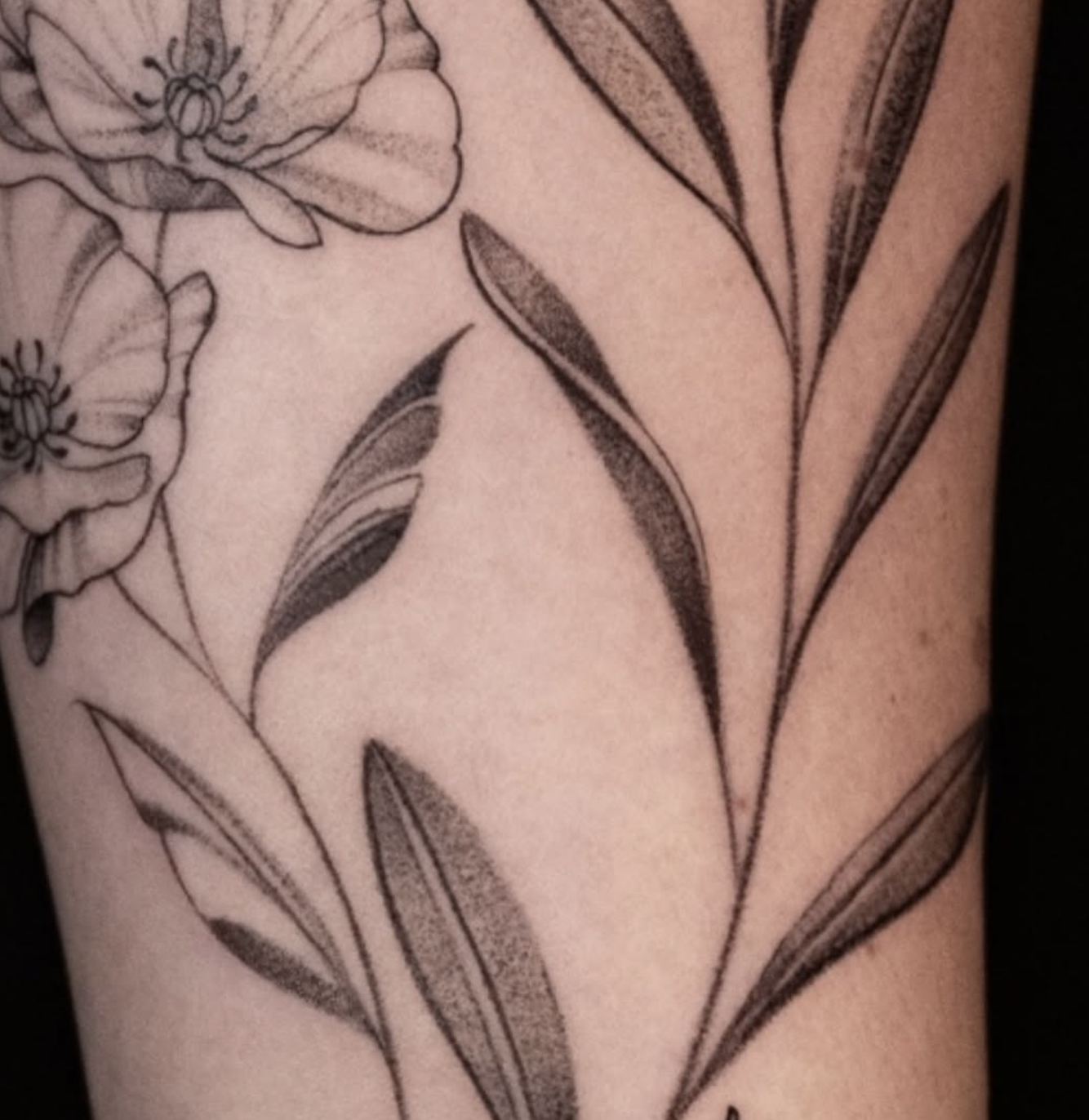 Close-up of a floral tattoo on skin, featuring detailed flowers and leaves with shading.