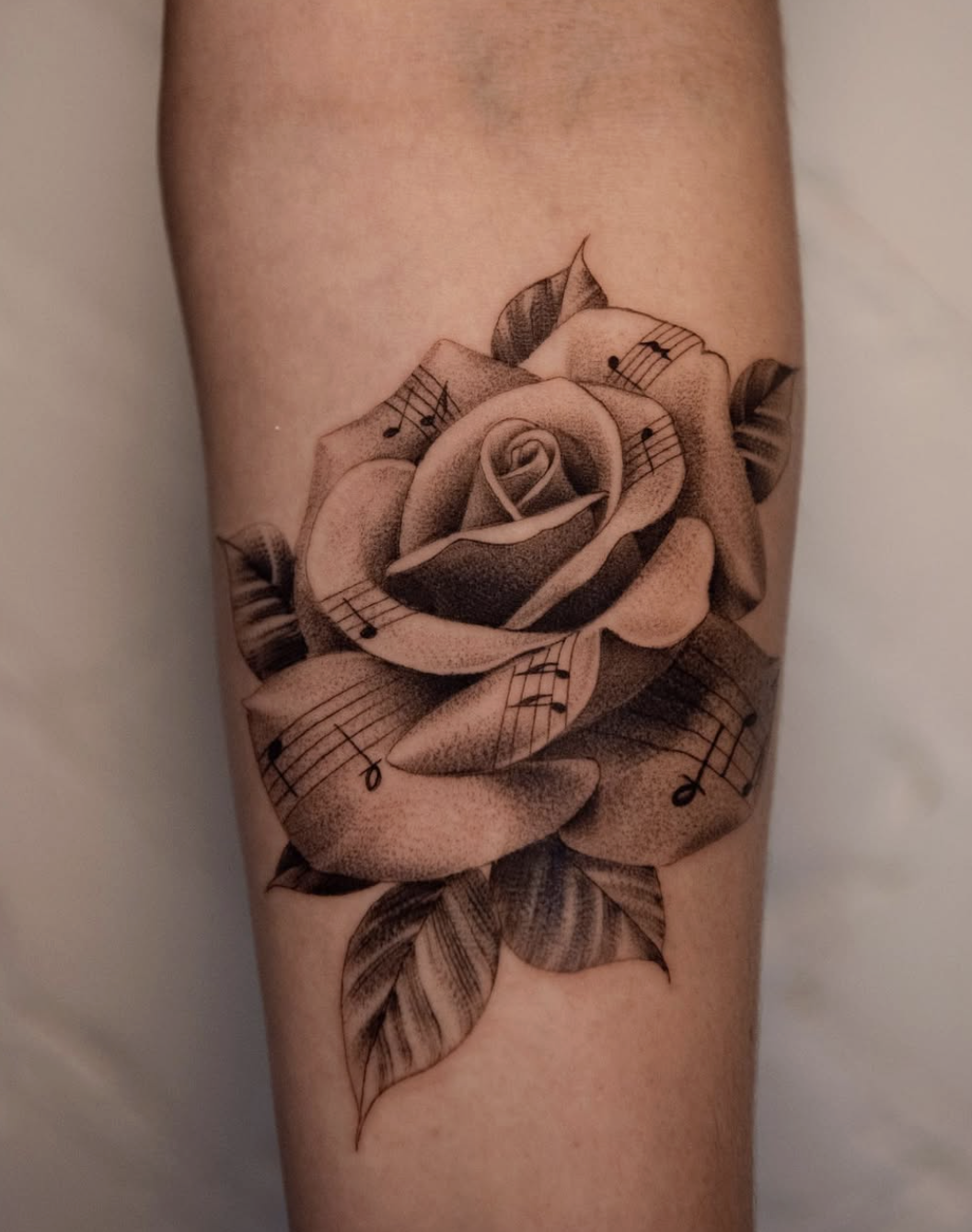 Tattoo of a rose with musical notes on its petals and leaves.