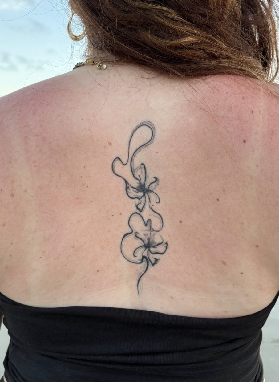 Tattoo of two hibiscus flowers with long, curving stems centered on a woman's upper back.