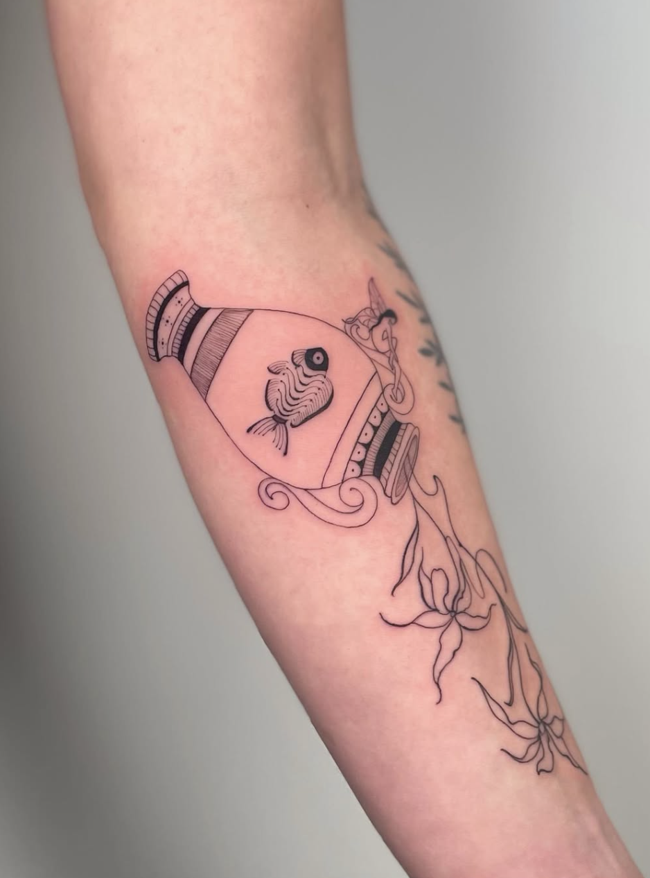Line art tattoo of a fishbowl with a fish inside, a unicorn head, and floral elements on a person's arm.