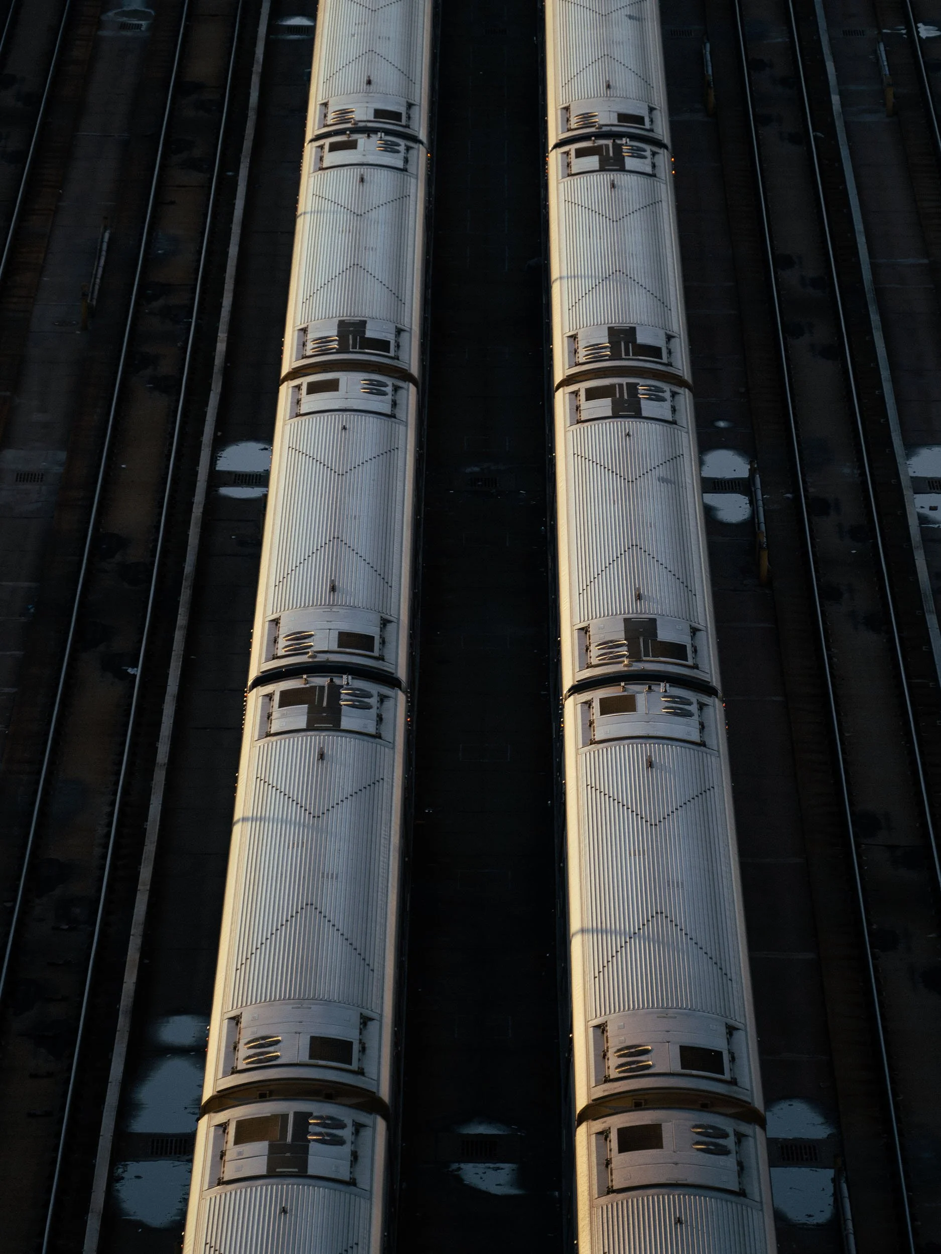 Top-down aerial view of train cars parked on train tracks at a train station or yard during dusk or dawn.