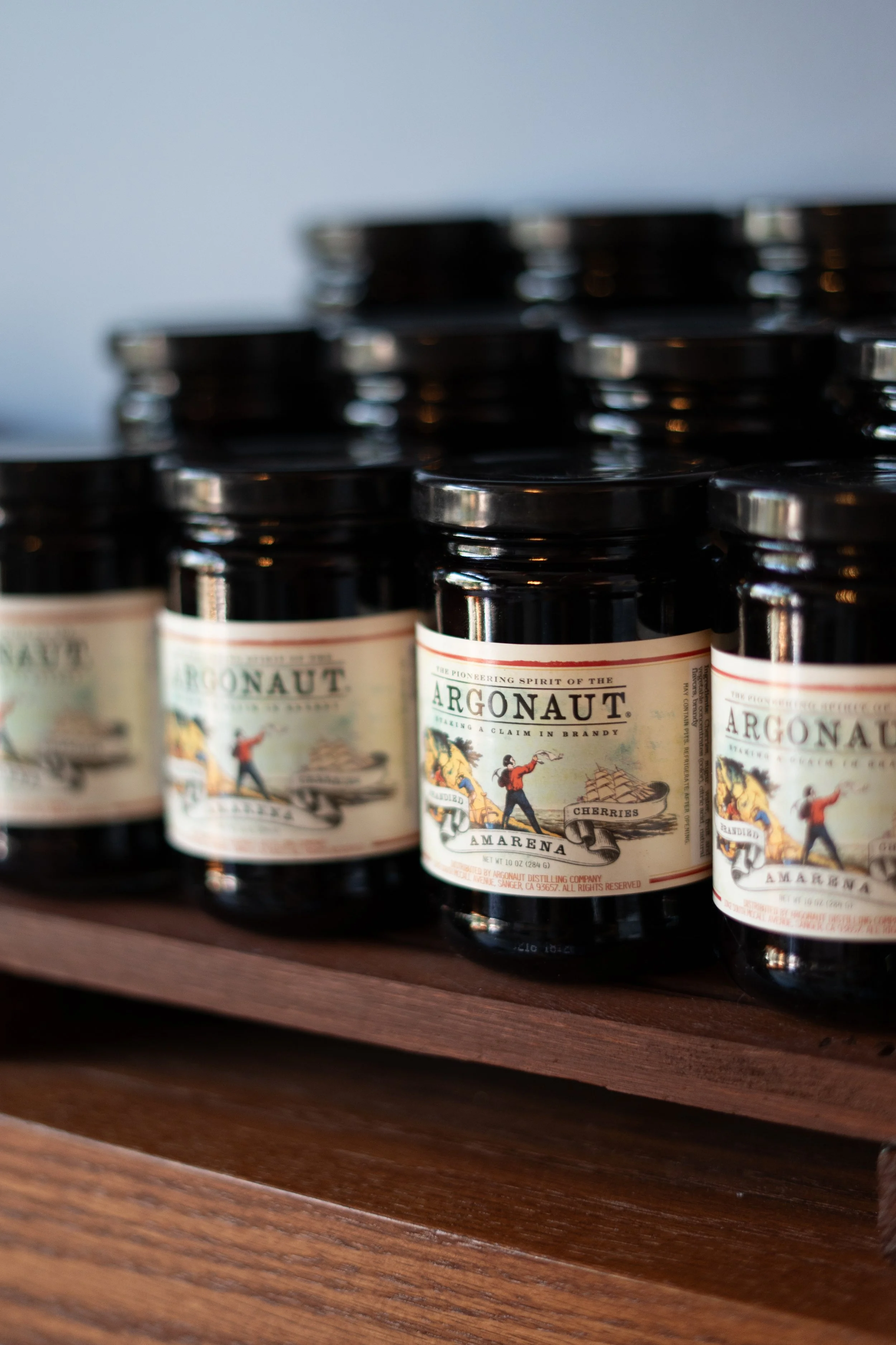 Close-up of bottles of Argonaut Amarena cherries on a wooden shelf.