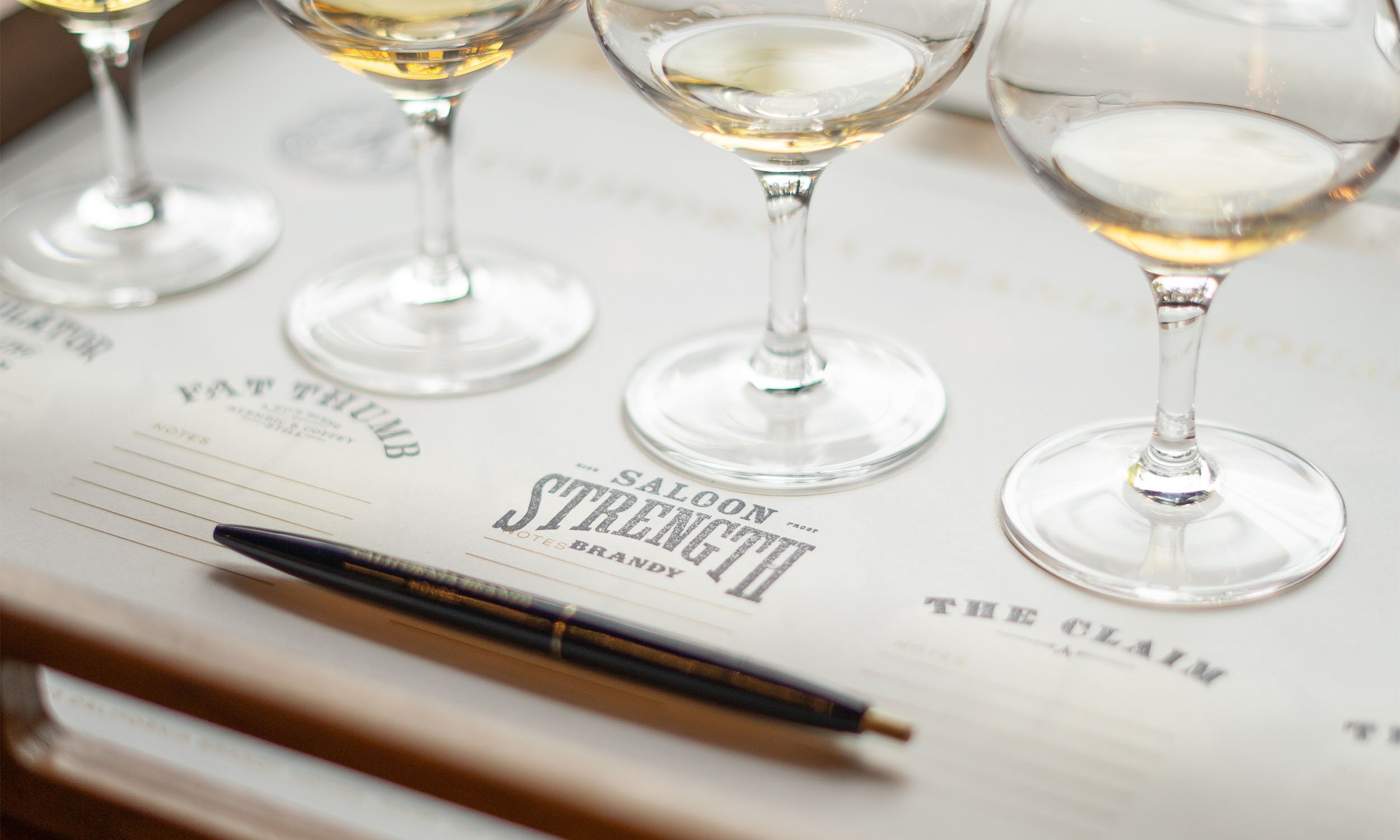 Several glasses of white wine on a tray with a notepad, pen, and a menu card that reads 'Saloon Street'