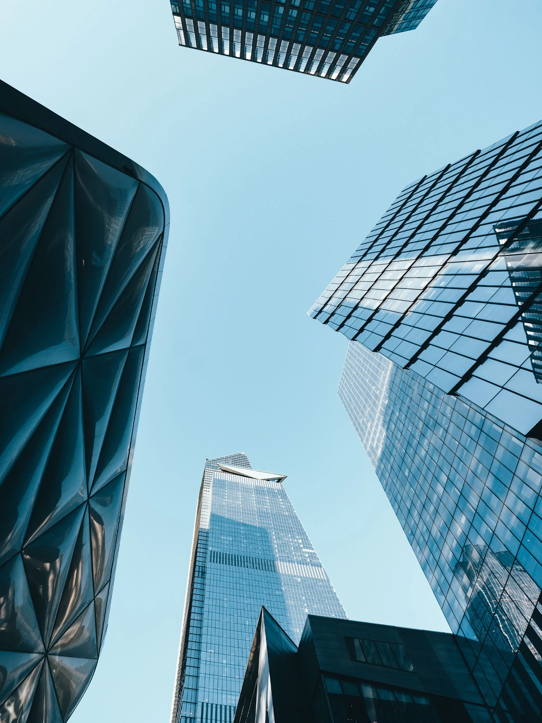 View looking up at tall modern glass skyscrapers against a clear blue sky.