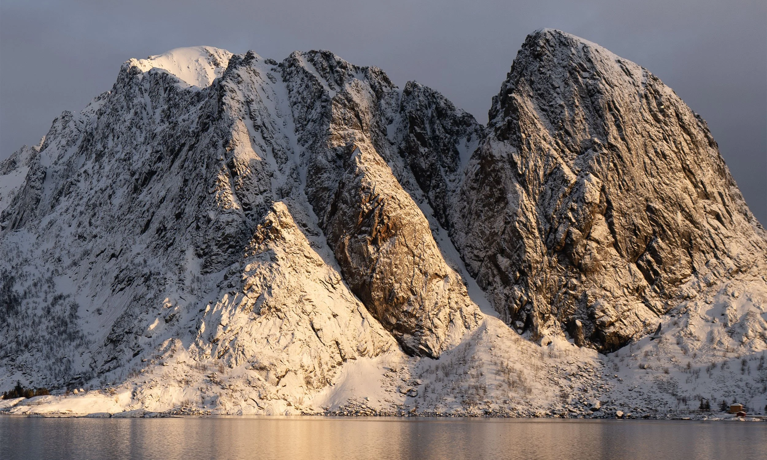 Snow-covered mountain peaks beside a calm body of water.