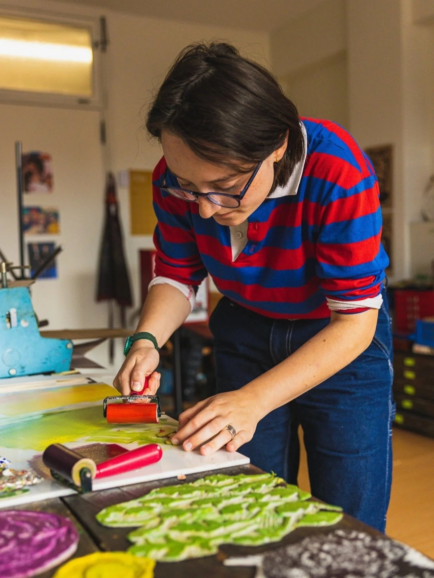Person using a roller to print or create a design on fabric or paper in an art studio.