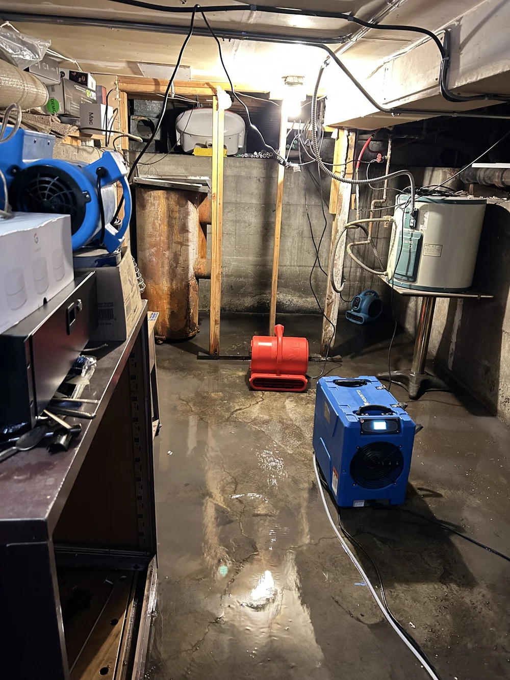 Basement with wet concrete floor, dehumidifier, and fan.