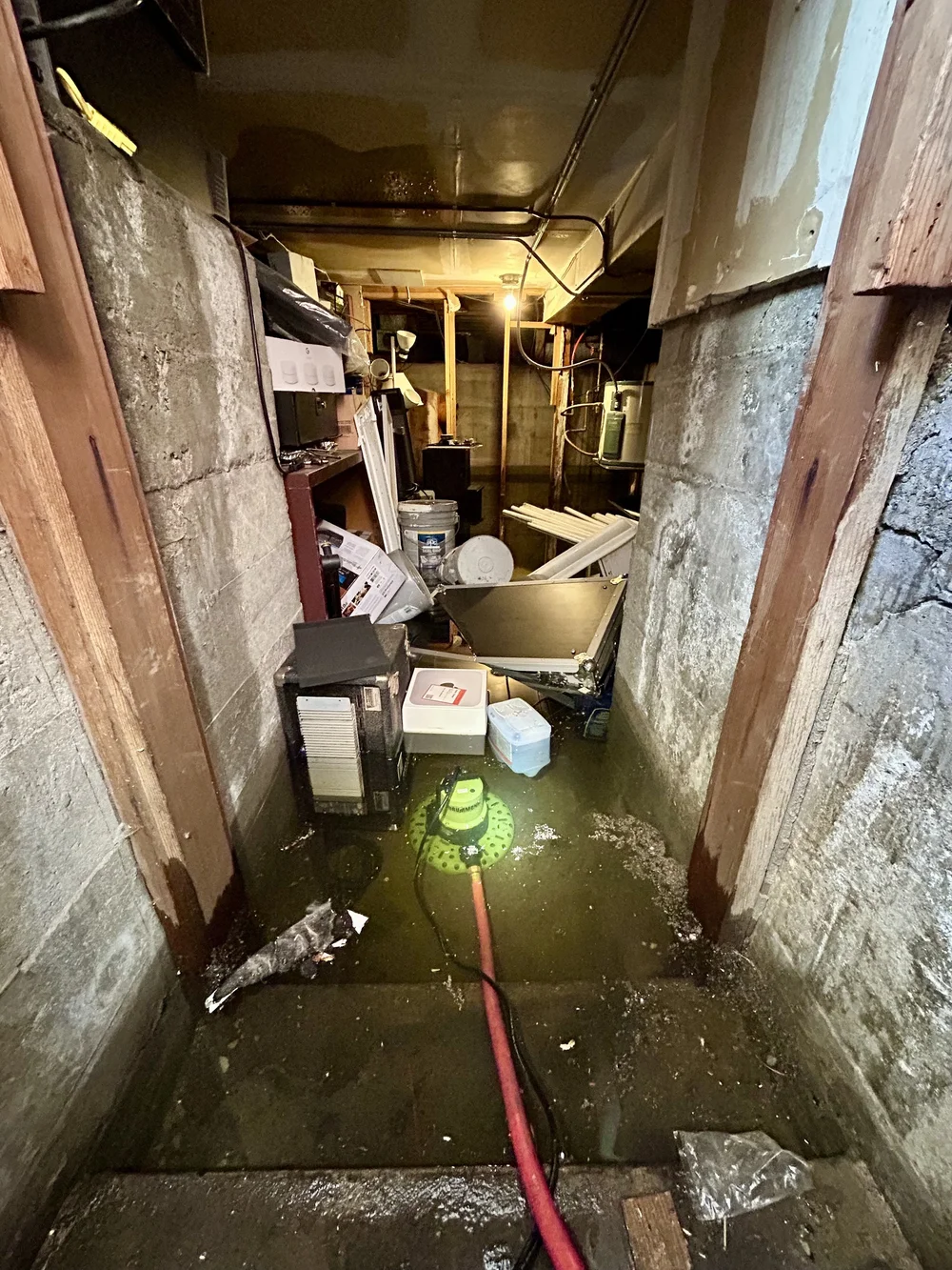 Basement flooding with water on the floor, tools, boxes, and debris.