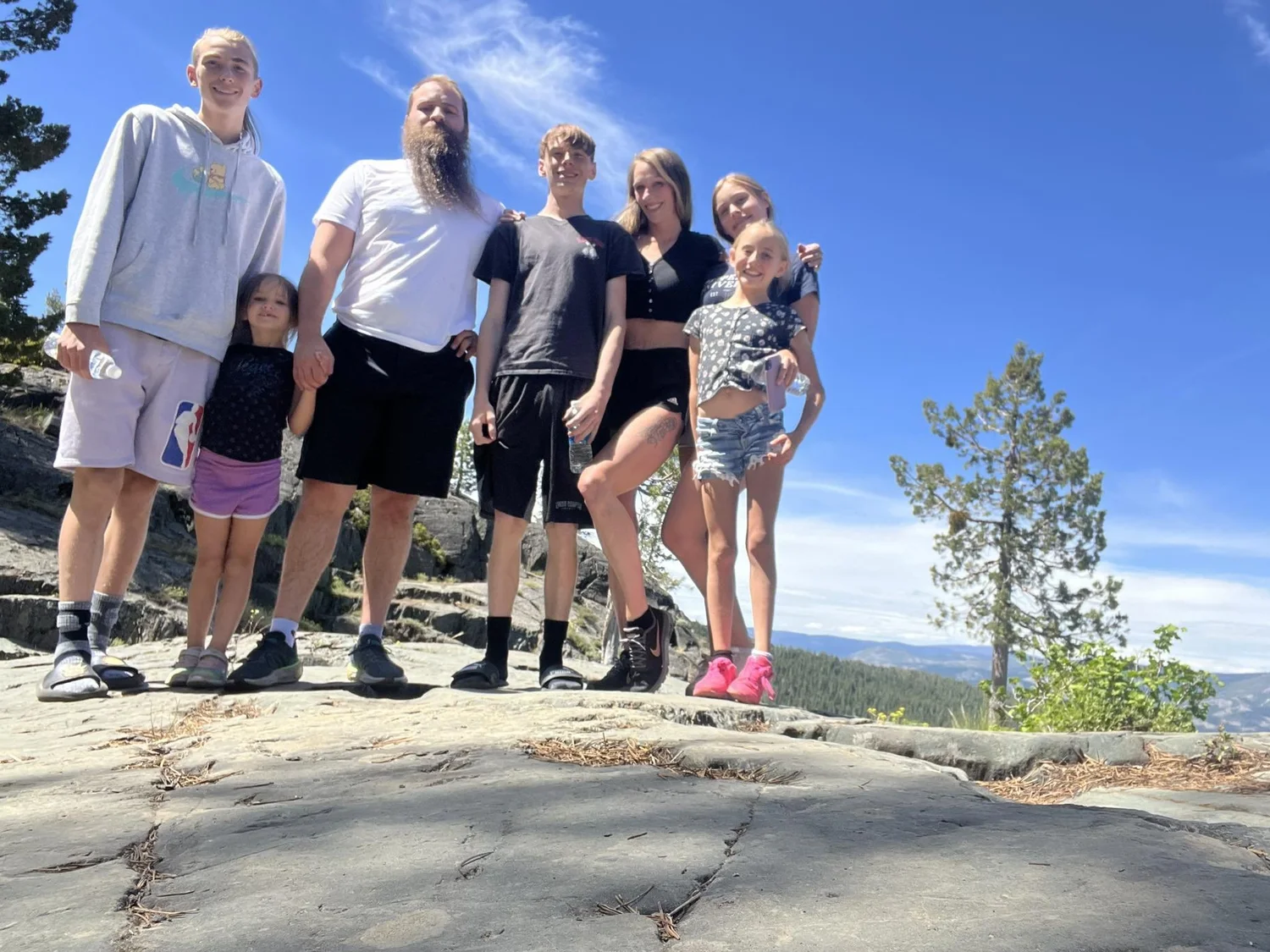 The family behind Sierra Water & Mold Recovery, eight adults and children outdoors with trees and mountains behind them.