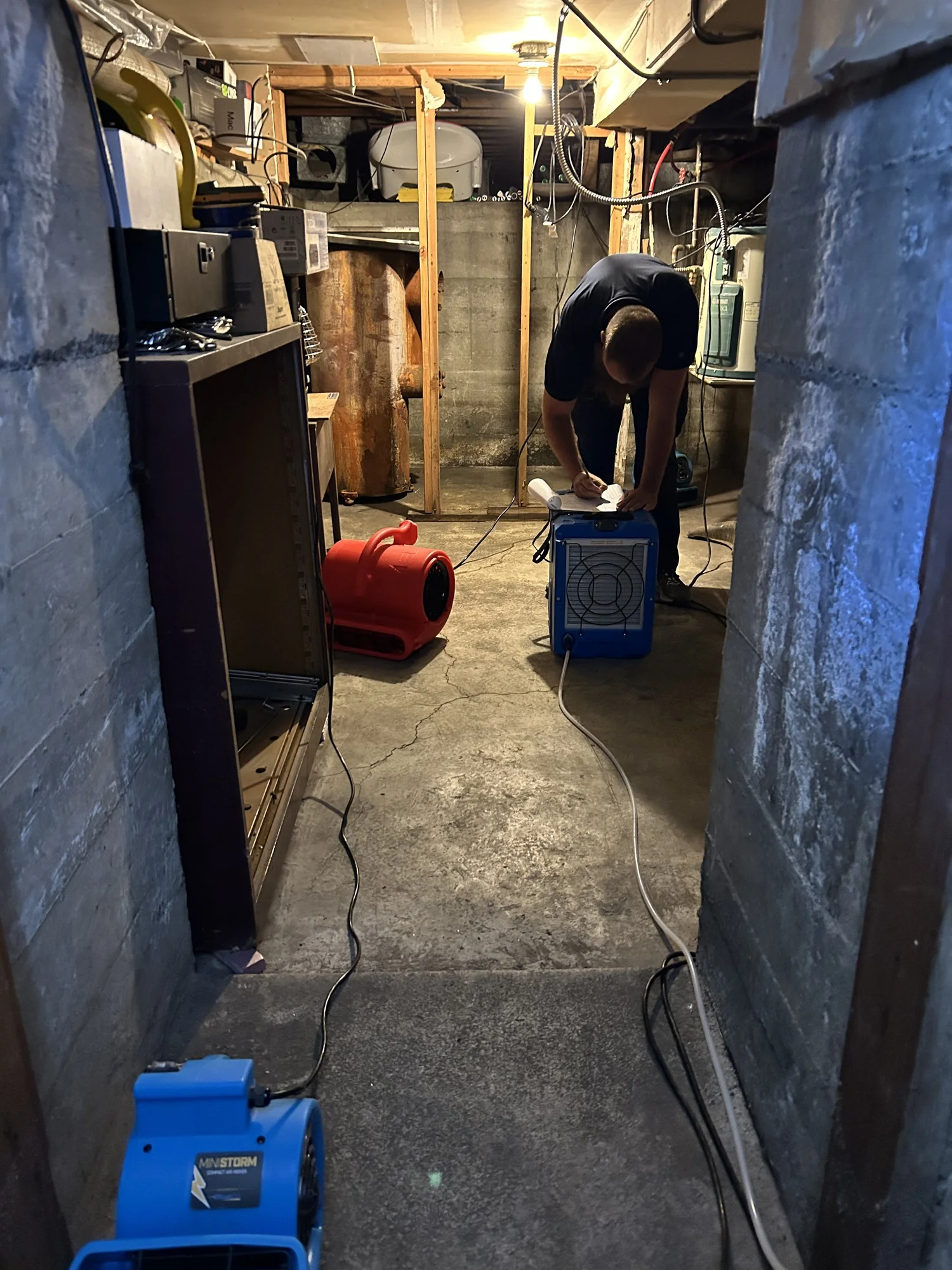 A Sierra technician working in a basement utility room with drying equipment.