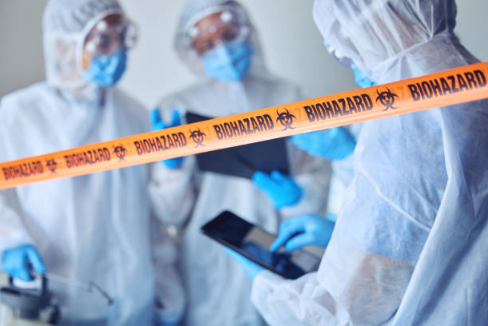An image of biohazard tape at forefront and defocused professional cleanup service crew members behind it