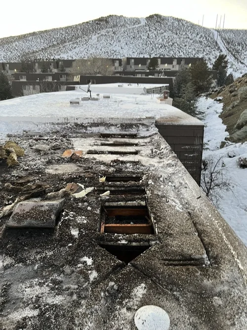 Damaged roof with snow, overlooking a snowy landscape with mountains in the background.