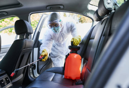 Image of a man in a hazmat suit leaned into a vehicle with leather interior sanitize spraying the interior