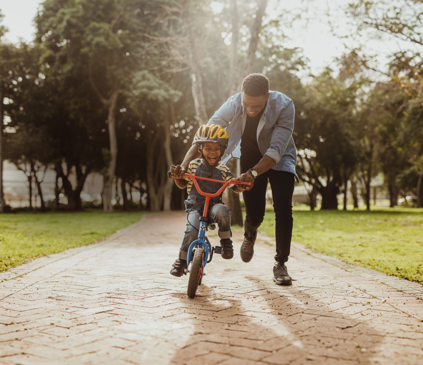 Father teaching his child to ride a bike along a sunlit path at Austin Point