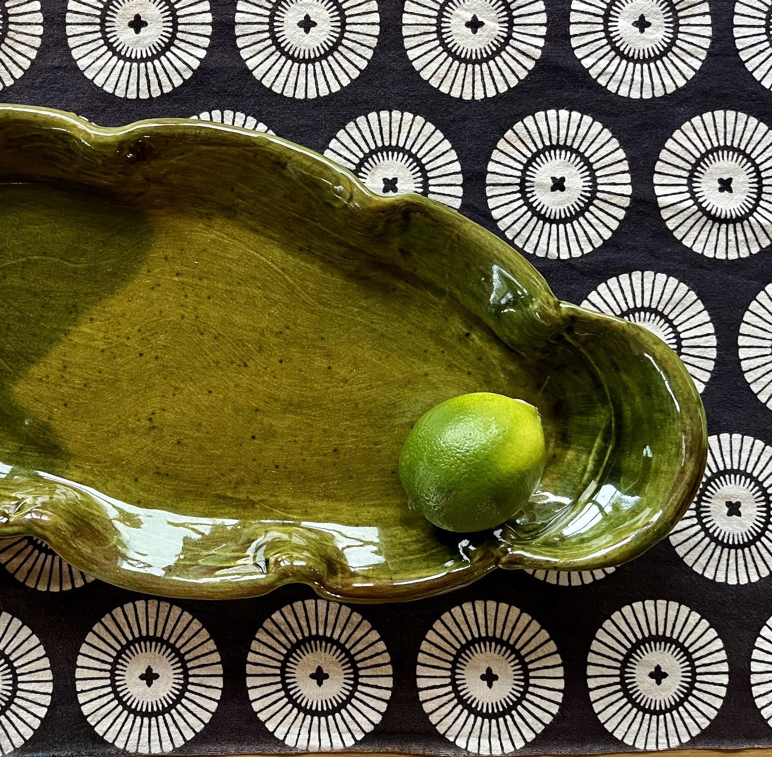 Green lime on a decorative green ceramic plate with a black and white circular patterned background.