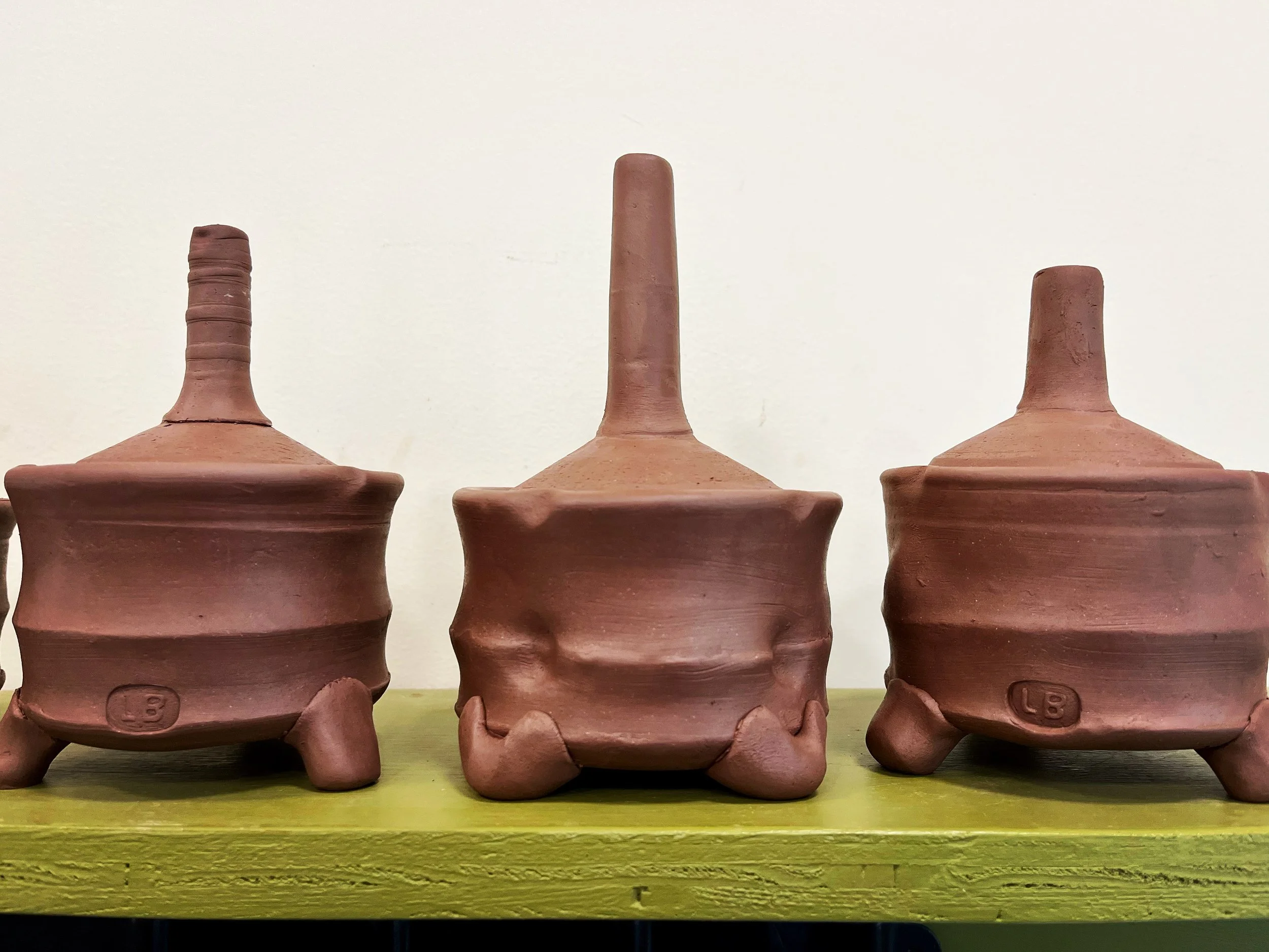 Three handcrafted clay pots with unique lids on a green surface