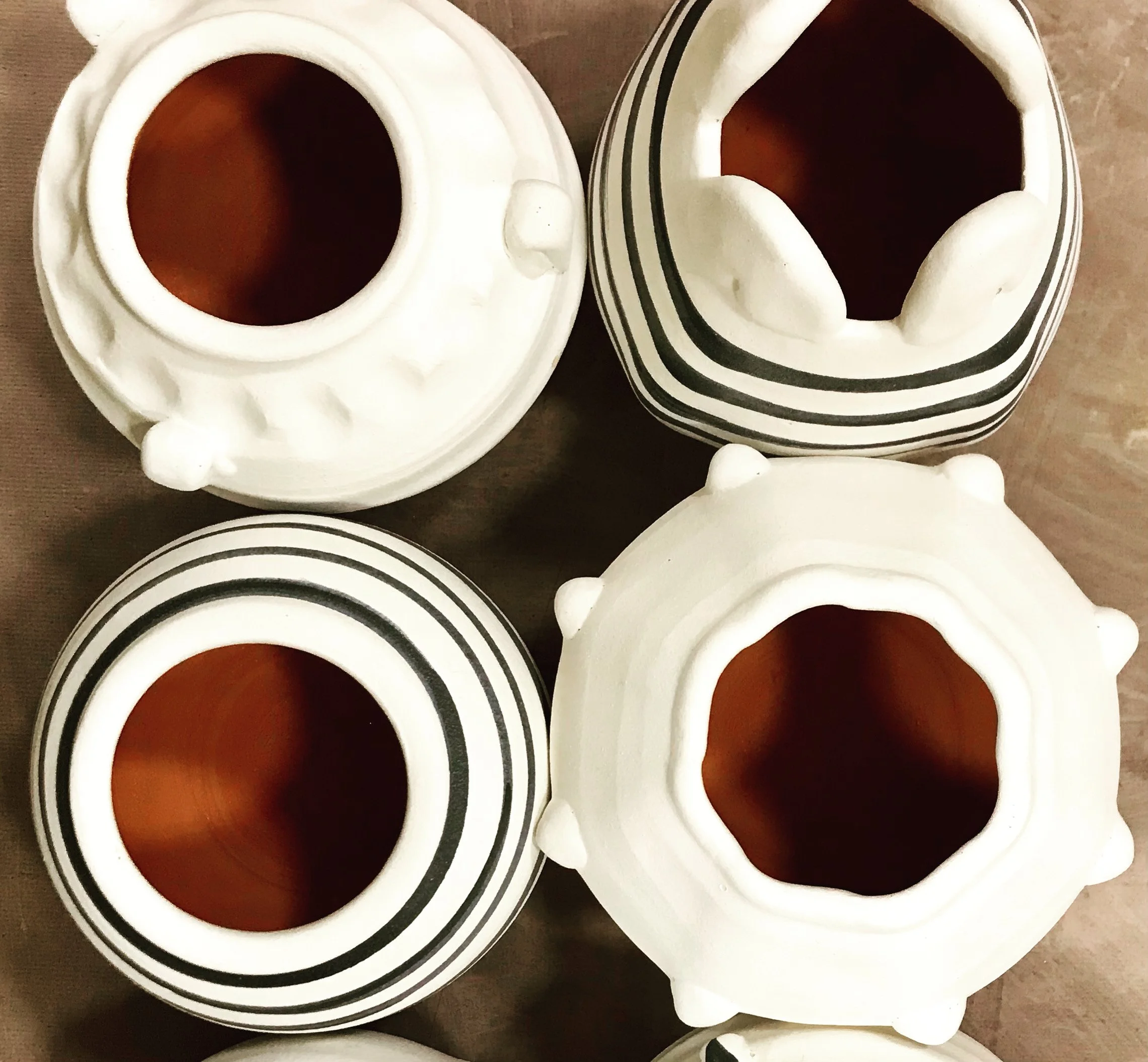 Top view of five ceramic pots with white exteriors and black striped patterns, featuring wide openings and textured surfaces.