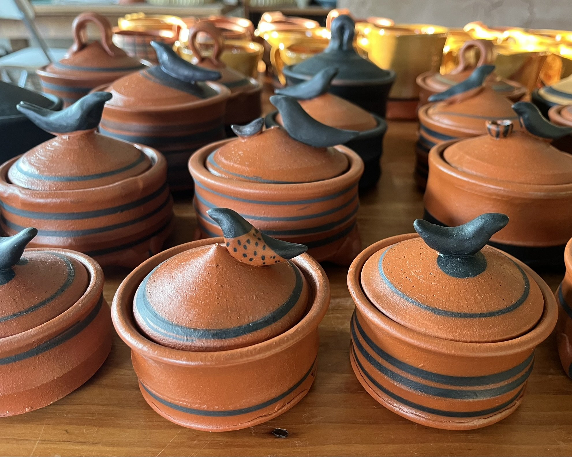 Clay pots with lids, featuring bird-shaped handles, arranged on a wooden surface.