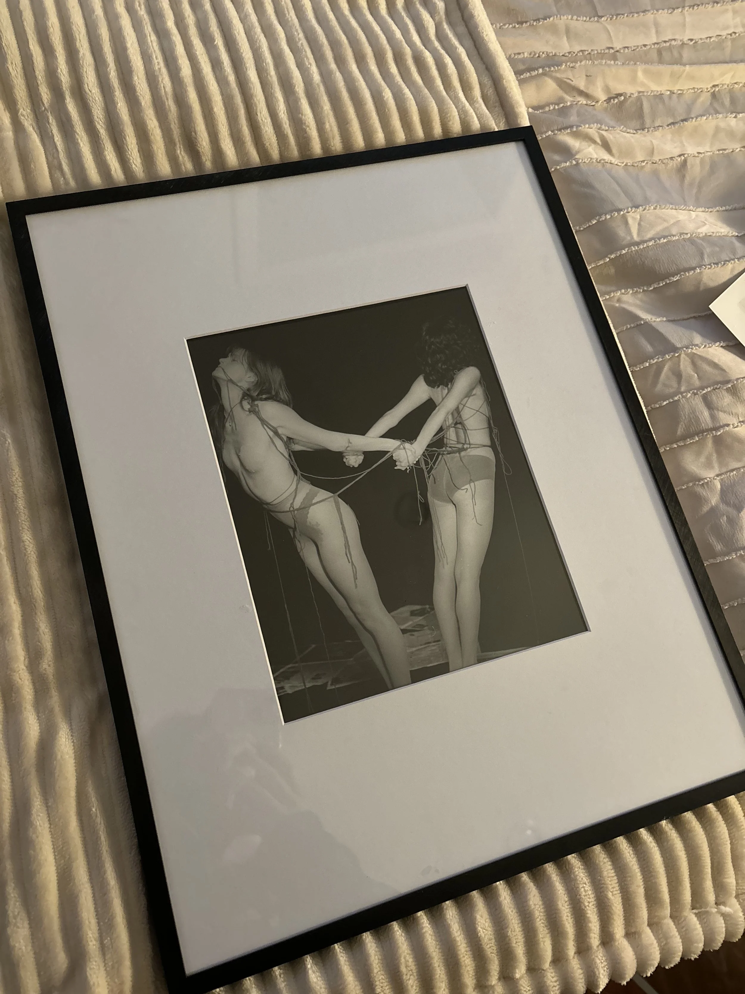 A framed picture of two women holding each other while tied together via threads.