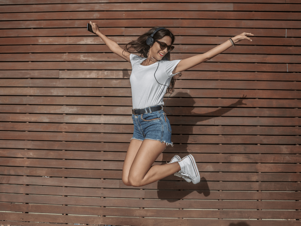 A woman airborne with headphones, expressing exhilaration and mania through her dynamic jump.